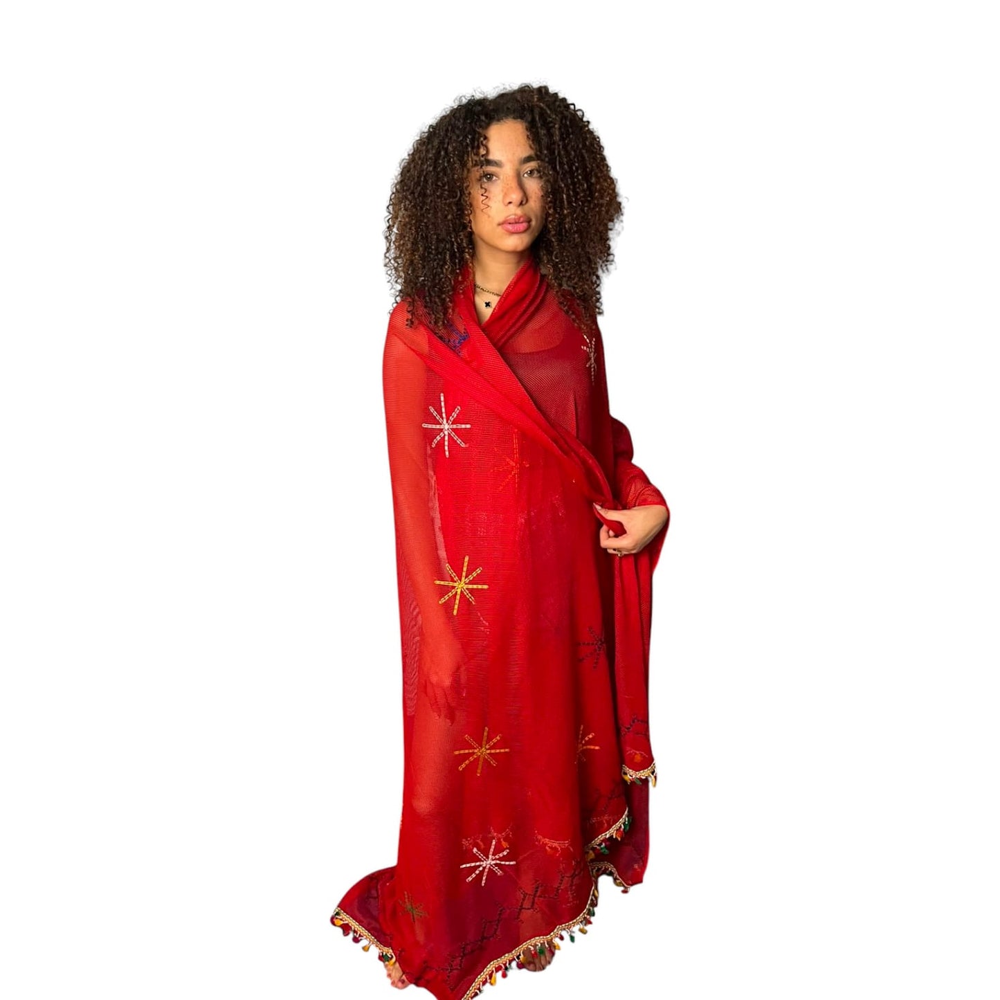 A woman wearing a red large scarf with hand-embroidered details and a colorful fringe, posing against a white background.