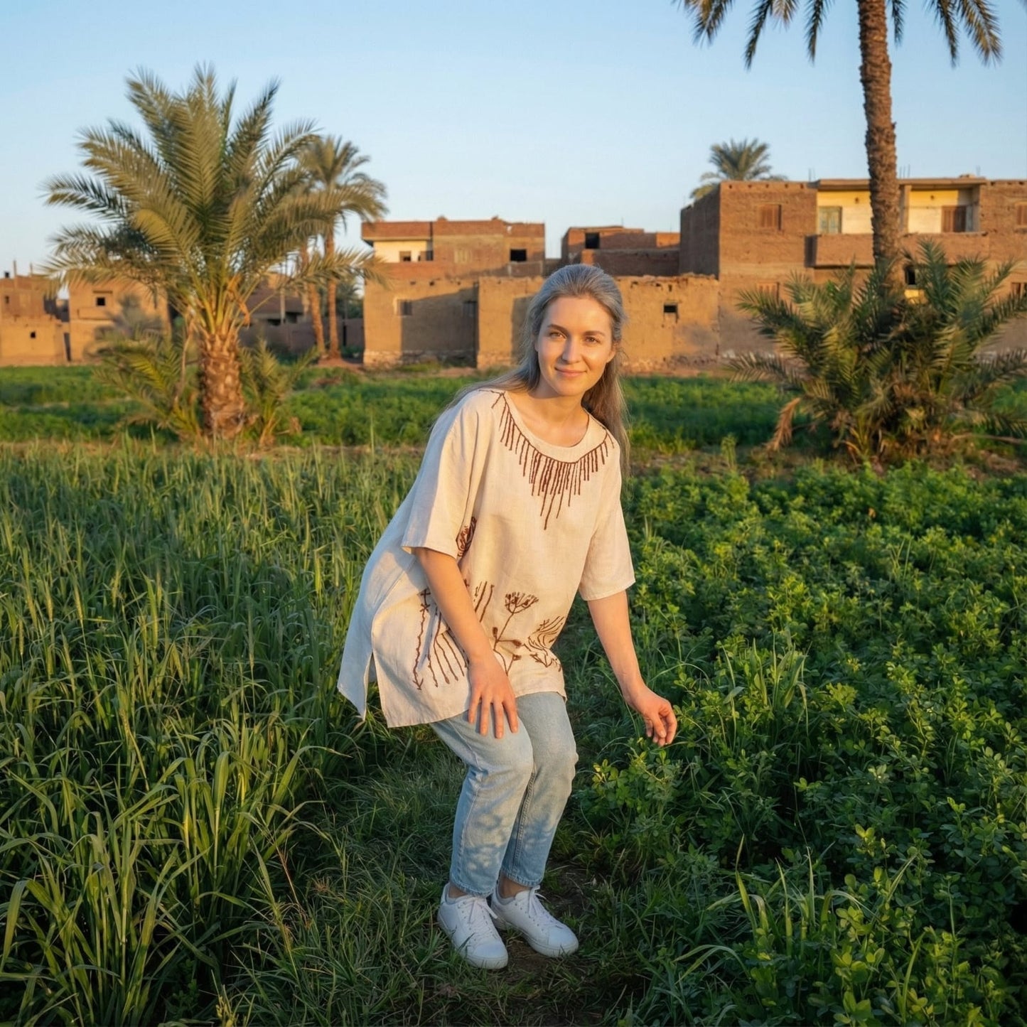 Woman standing in a field with traditional buildings and palm trees in the background