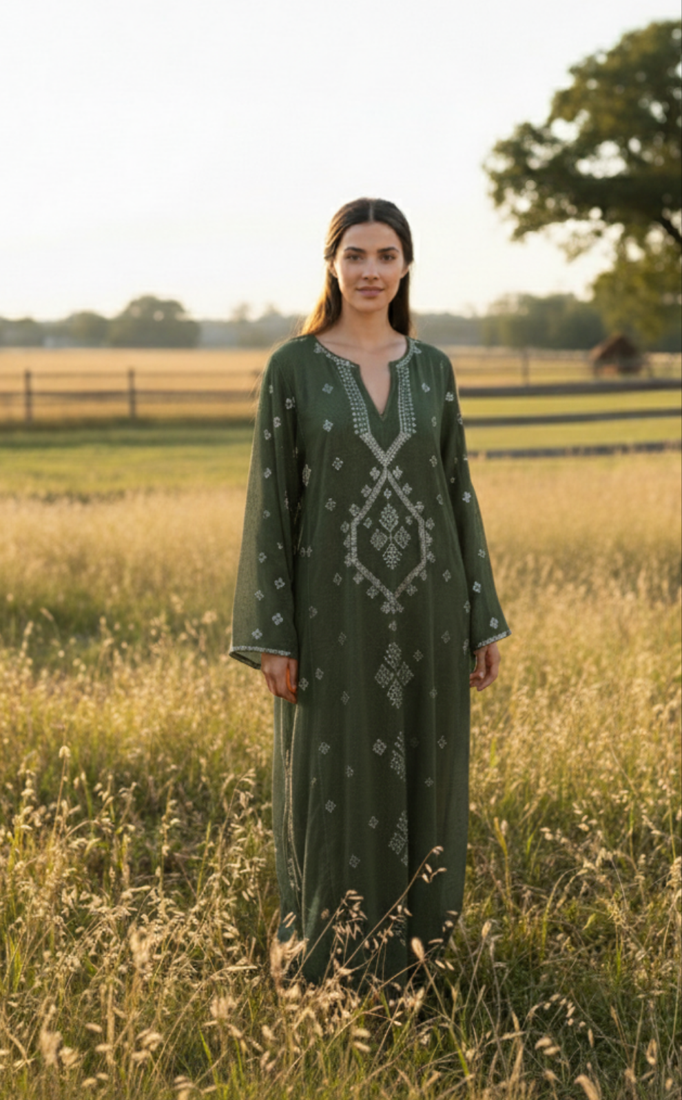 Woman in a green dress standing in a field with trees in the background