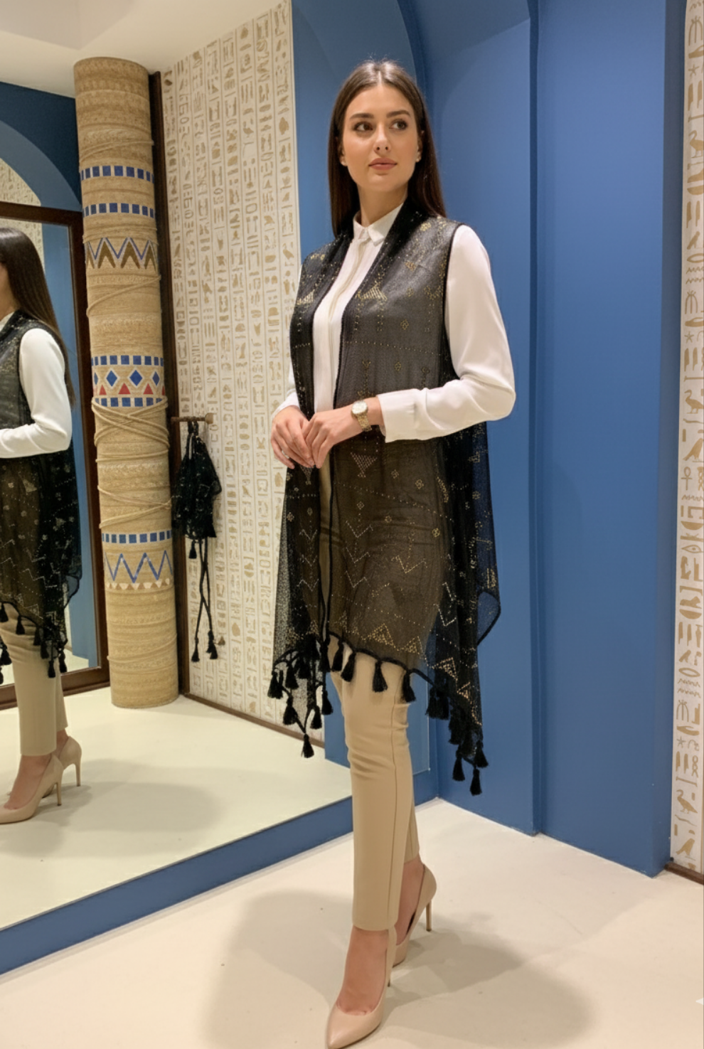 Woman wearing a black patterned Tally vest over a white shirt and beige pants in a store setting.