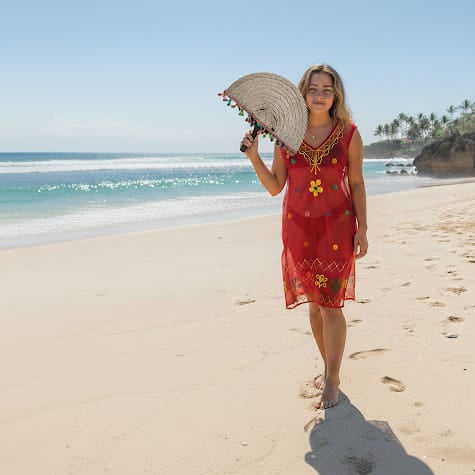 Woman in a red dress holding a straw hat on a beach with palm trees in the background