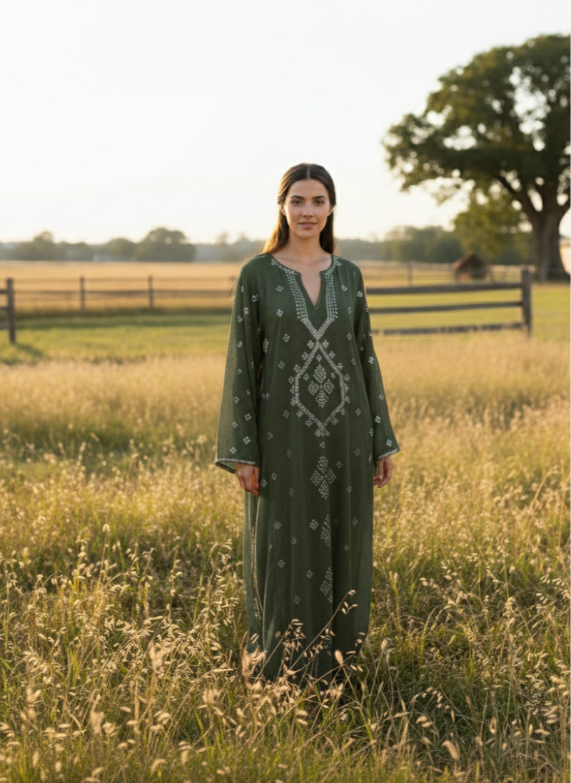 Woman in a green dress standing in a field with a fence and trees in the background