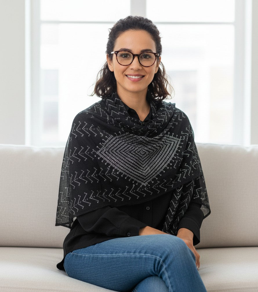 Woman wearing a black patterned shawl sitting on a white couch.