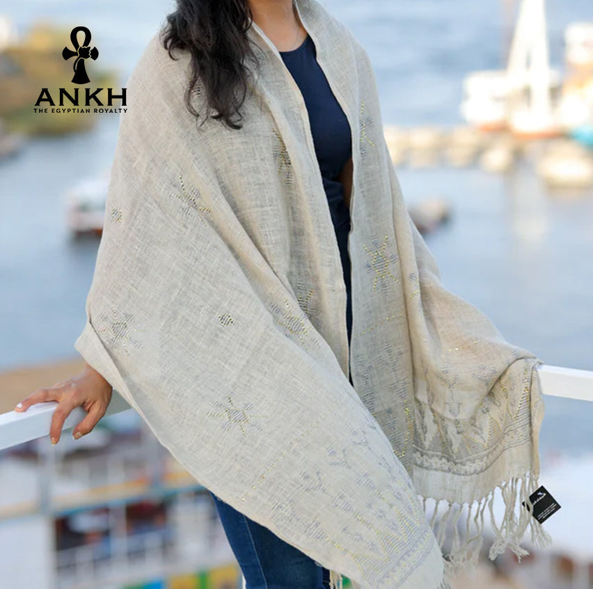 A woman wearing a black and white scarf with Egyptian symbols on it. The woman is standing on a balcony overlooking the sea.