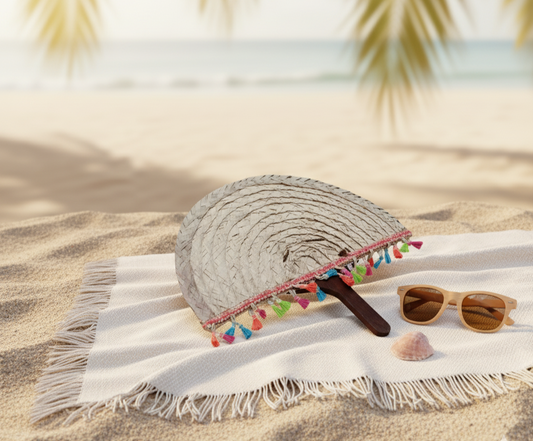 Beach towel with a paddle and sunglasses on sand with palm leaves in the background