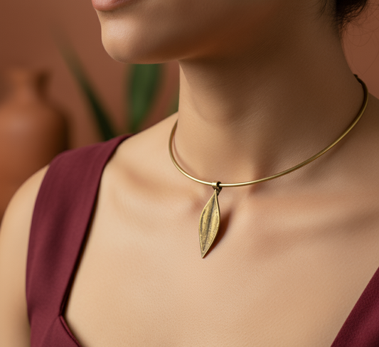 Close-up of a person wearing a gold necklace with a leaf pendant against a blurred background.