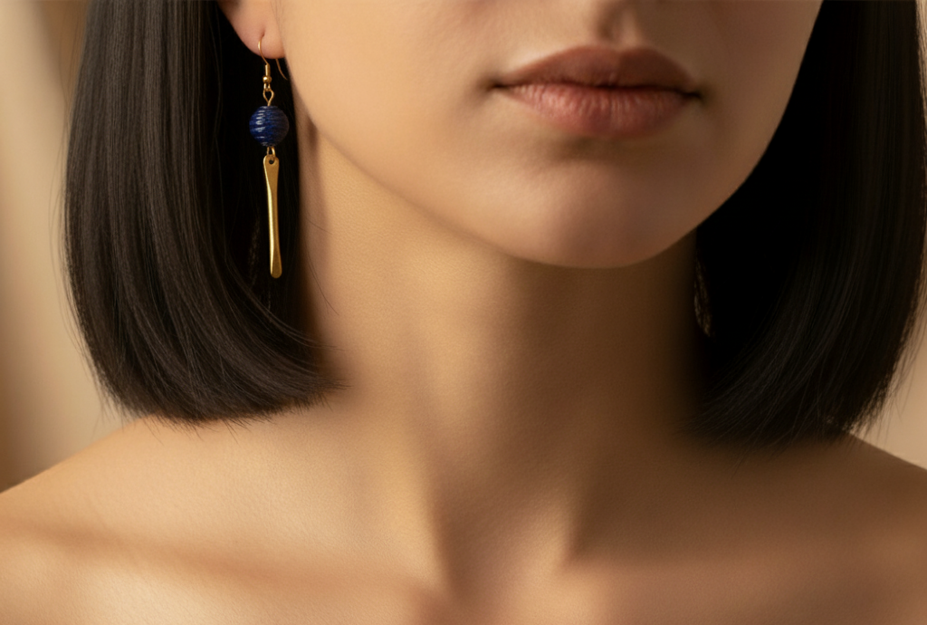 Close-up of a person wearing gold and blue earrings with a neutral background
