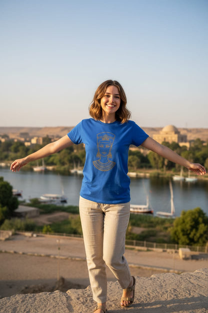 Woman wearing a blue t-shirt with a logo, standing outdoors with a scenic background.