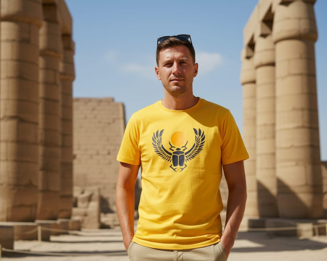 Man wearing a yellow t-shirt with a scarab design in front of ancient temple columns.
