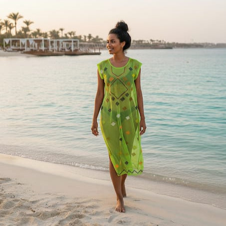Woman in a green dress walking on a beach with water and palm trees in the background