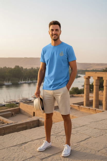 Man in a blue t-shirt and beige shorts standing in front of ancient ruins with a body of water in the background.