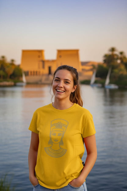 Woman wearing a yellow t-shirt with a design, standing by a body of water with a building in the background.