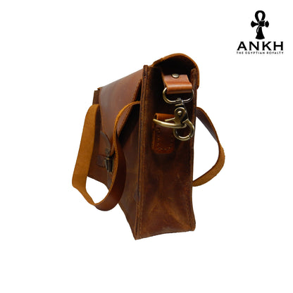 A genuine leather cross bag with handcrafted brass accessories and multiple pockets, displayed on a white background with a black logo of ANKH - The Egyptian Royalty.