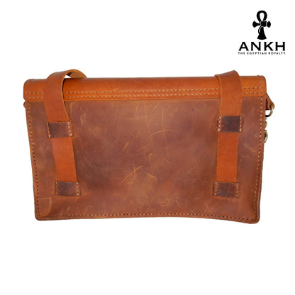 A genuine leather cross bag with handcrafted brass accessories and multiple pockets, displayed on a white background with a black logo of ANKH - The Egyptian Royalty.