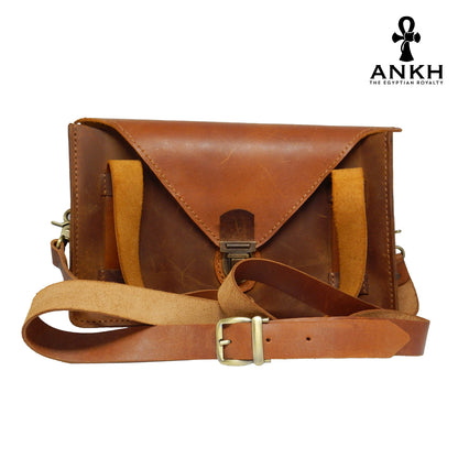 A genuine leather cross bag with handcrafted brass accessories and multiple pockets, displayed on a white background with a black logo of ANKH - The Egyptian Royalty.