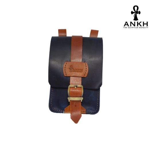 A genuine leather cross bag in dark blue with brown straps and handcrafted brass accessories, displayed on a white background with a black logo of ANKH - The Egyptian Royalty.