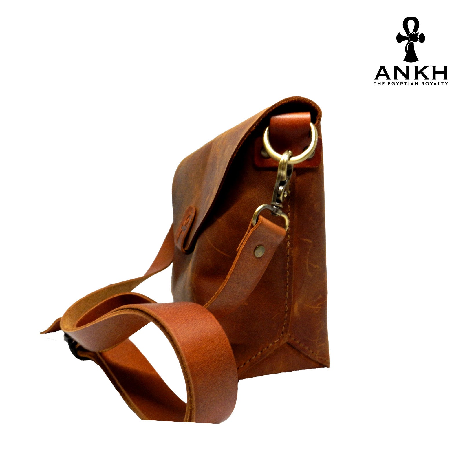 A genuine leather cross bag in red color with handcrafted brass accessories and multiple pockets, displayed on a white mannequin bust with a black logo of ANKH - The Egyptian Royalty.