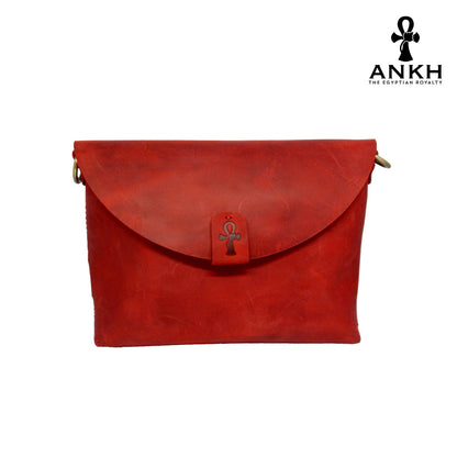 A genuine leather cross bag in red color with handcrafted brass accessories and multiple pockets, displayed on a white mannequin bust with a black logo of ANKH - The Egyptian Royalty.