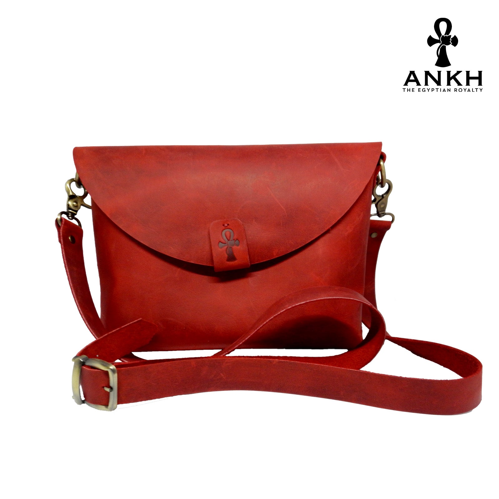 A genuine leather cross bag in red color with handcrafted brass accessories and multiple pockets, displayed on a white mannequin bust with a black logo of ANKH - The Egyptian Royalty.