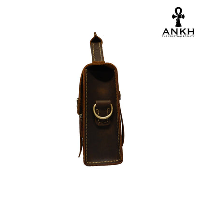 A genuine leather cross bag with handcrafted brass accessories and multiple pockets, displayed on a white background with a black logo of ANKH - The Egyptian Royalty.