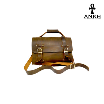 A genuine leather cross bag with handcrafted brass accessories and multiple pockets, displayed on a white background with a black logo of ANKH - The Egyptian Royalty.