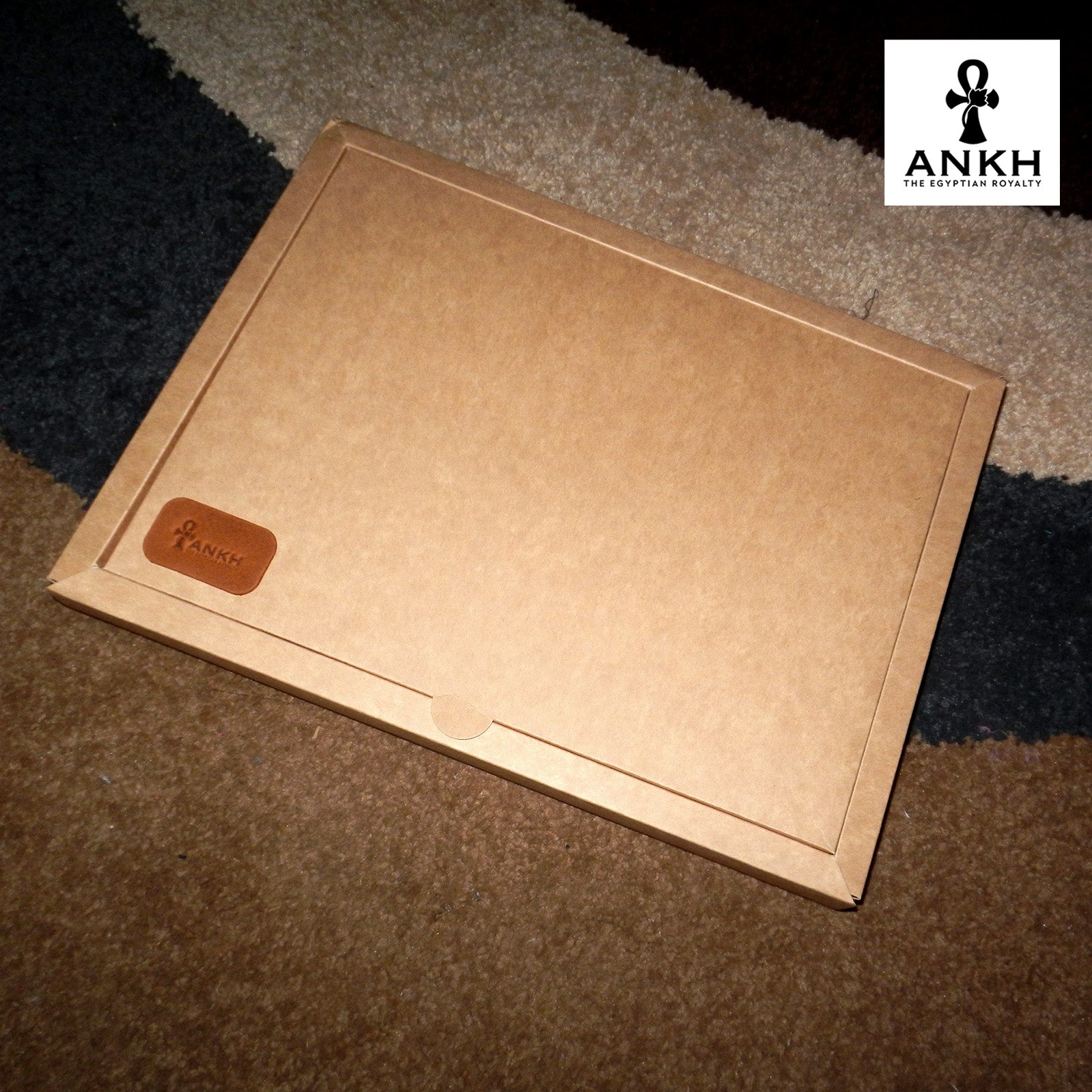 A white box containing four ANKH leather accessories: a passport cover with notebook, a key chain, a glasses cover, and a card holder, displayed on a textured surface. طقم هدية من الجلد الطبيعي الفاخر منقوش برمز العنخ المصري هدية من مصر