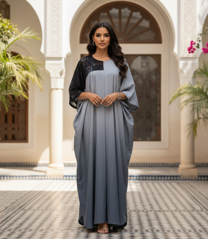Woman in a long, light blue dress with black lace sleeves standing in a decorative courtyard.