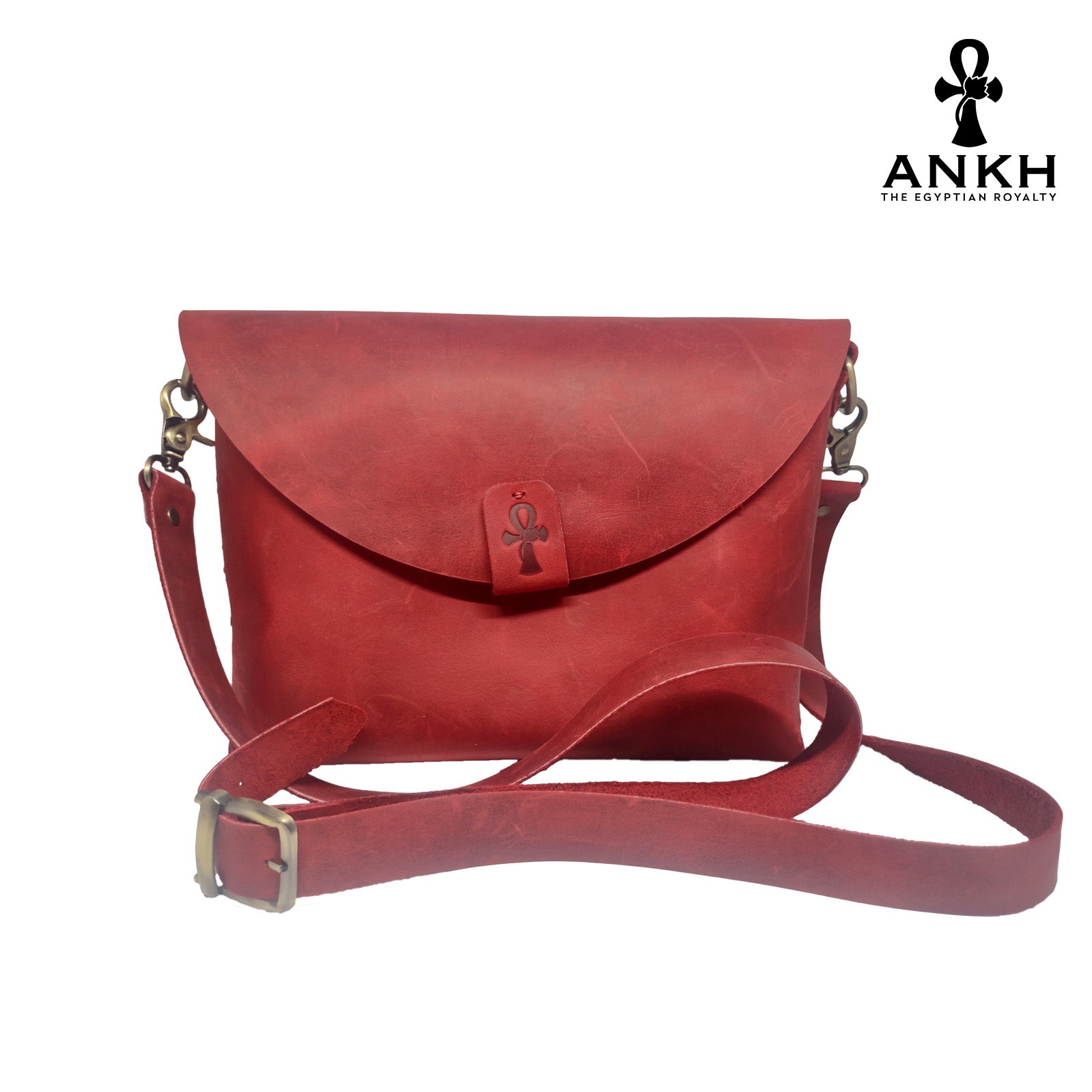 A genuine leather cross bag in red color with handcrafted brass accessories and multiple pockets, displayed on a white mannequin bust with a black logo of ANKH - The Egyptian Royalty.