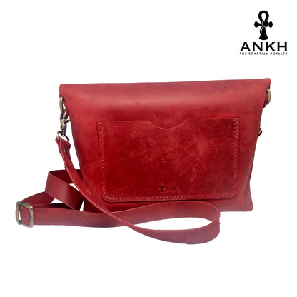 A genuine leather cross bag in red color with handcrafted brass accessories and multiple pockets, displayed on a white mannequin bust with a black logo of ANKH - The Egyptian Royalty.