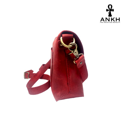 A genuine leather cross bag in red color with handcrafted brass accessories and multiple pockets, displayed on a white mannequin bust with a black logo of ANKH - The Egyptian Royalty.