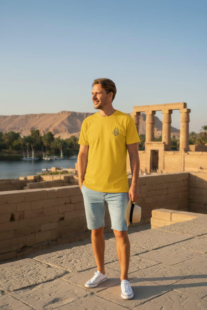 Man in a yellow t-shirt and light blue shorts standing in front of ancient ruins.