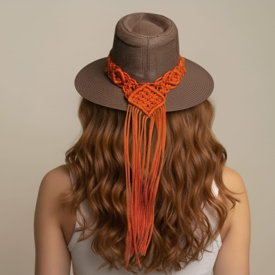 Brown hat with orange macramé details worn by a person with long hair on a beige background