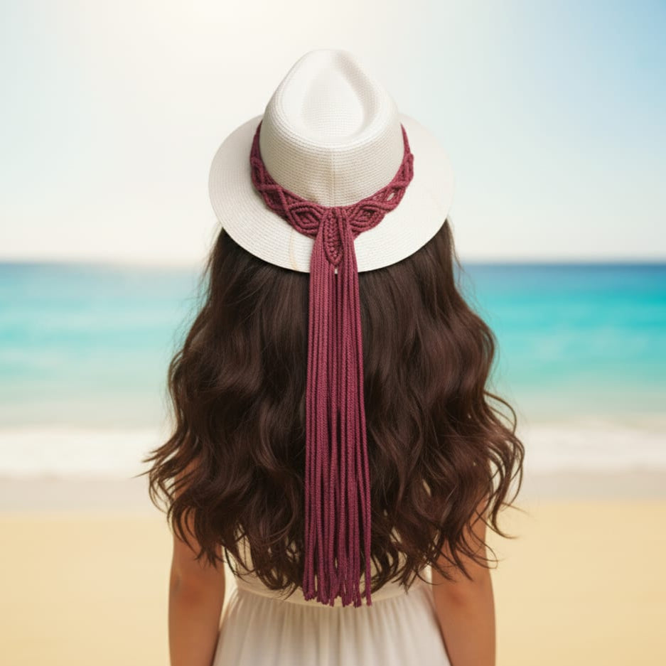 Person wearing a white hat with a red macramé ribbon on a beach
