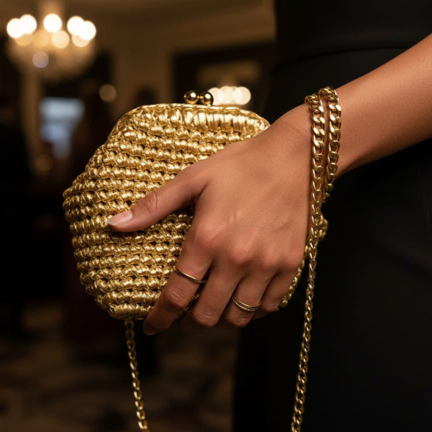 Gold handbag held by a person with a blurred indoor background