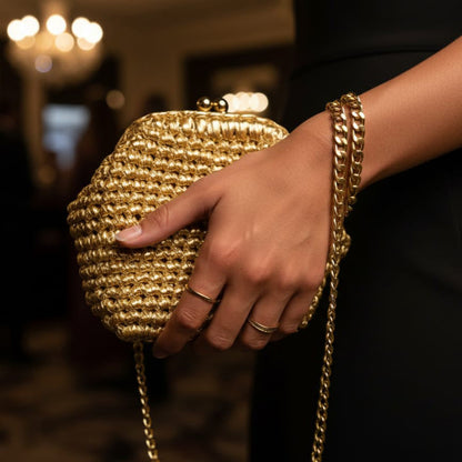 Gold handbag held by a person with a blurred indoor background