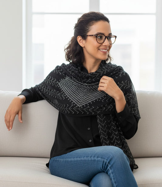 Woman wearing a black patterned shawl sitting on a couch.