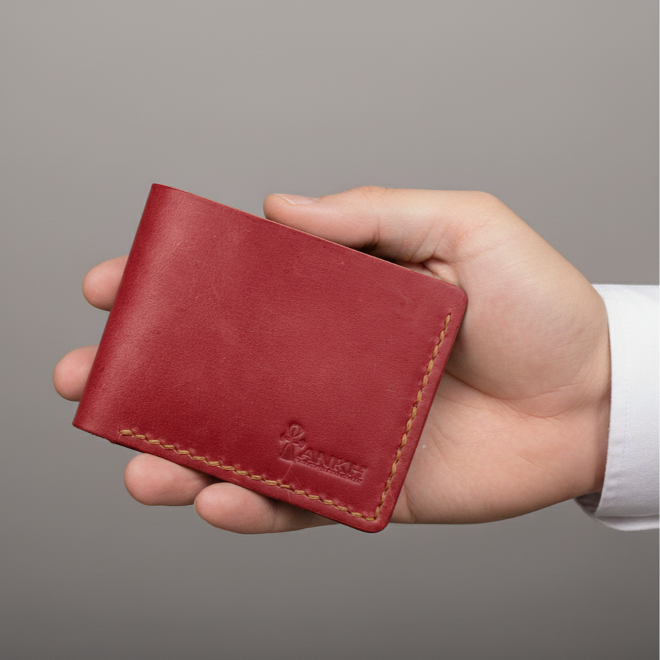 Hand holding a red leather wallet against a gray background