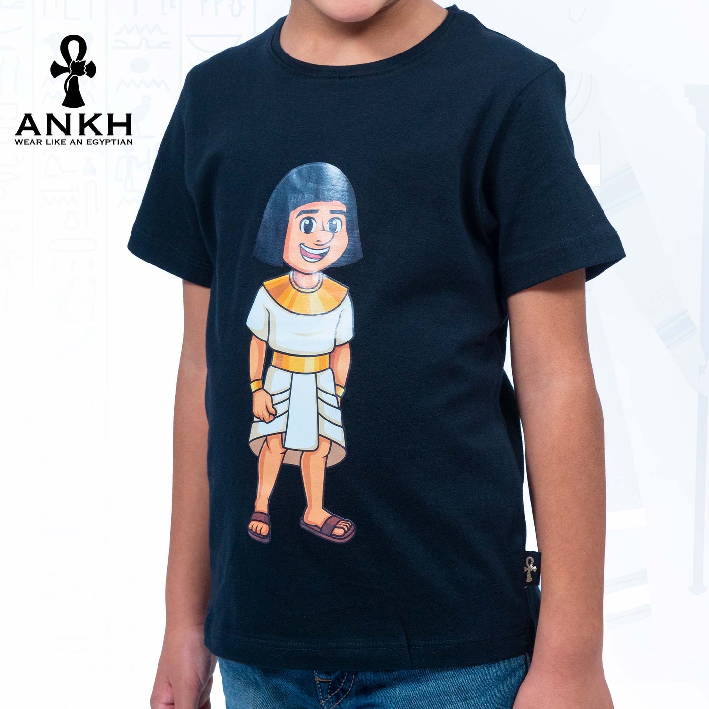 A child wearing a dark blue T-shirt adorned with a playful illustration of Sinuhe, an iconic Egyptian boy character - an epitome of luxury and cultural richness