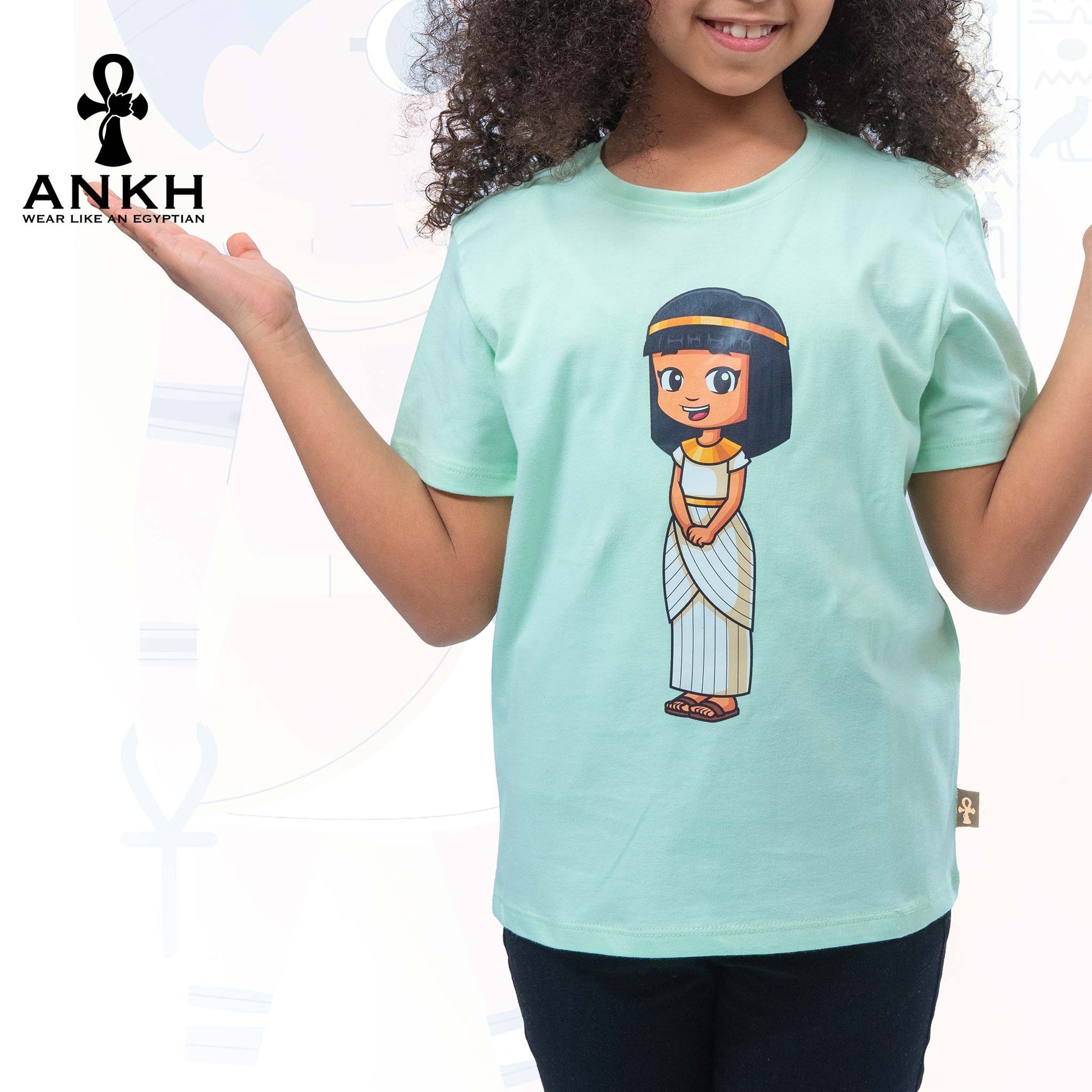 A child wearing Ankh’s cyan green t-shirt adorned with ‘Anippe’, a cartoony Egyptian girl character printed on premium quality 100% Egyptian cotton - perfect attire reflecting ancient Egyptian culture