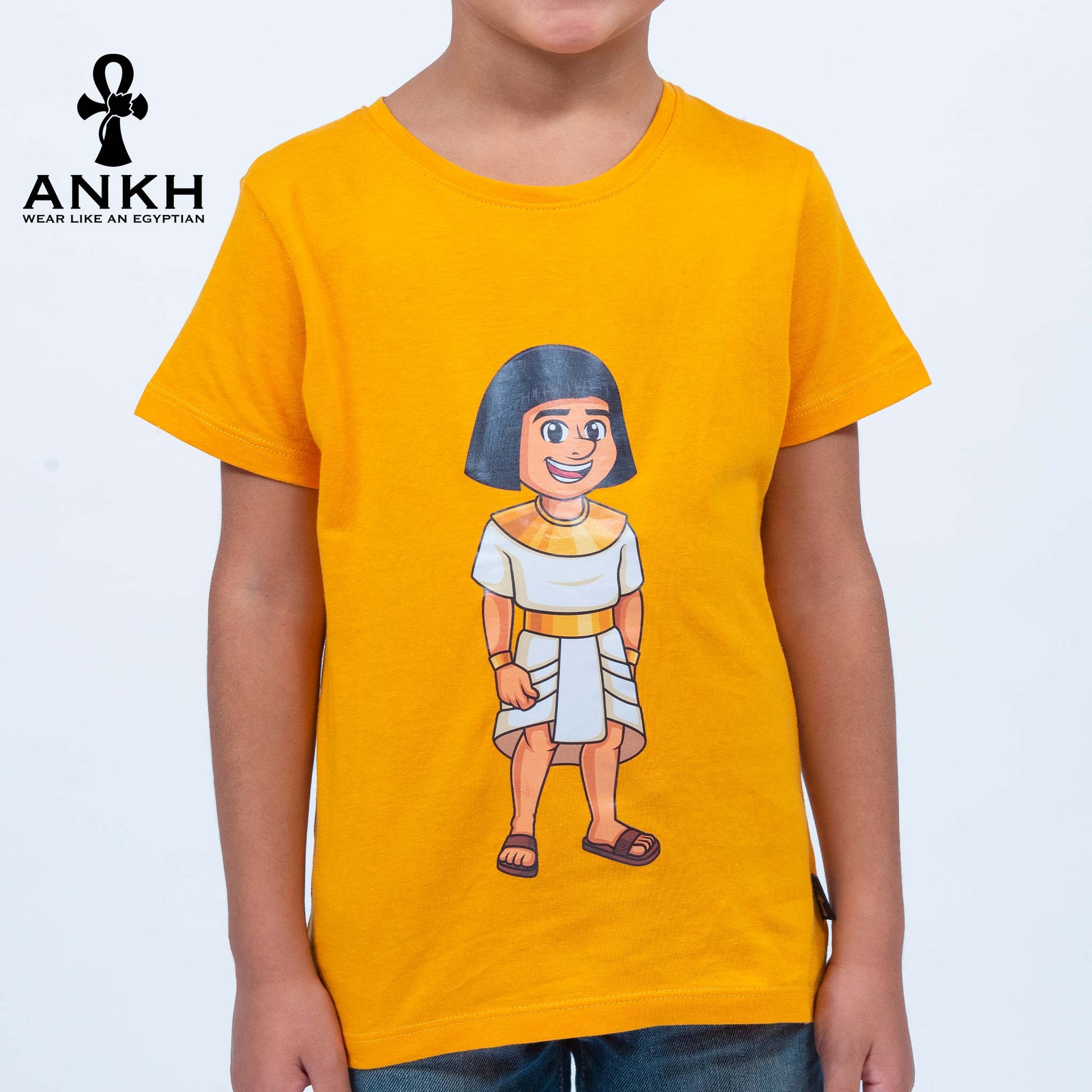 A child wearing a bright yellow T-shirt adorned with a playful illustration of Sinuhe, an iconic Egyptian boy character - an epitome of luxury and cultural richness