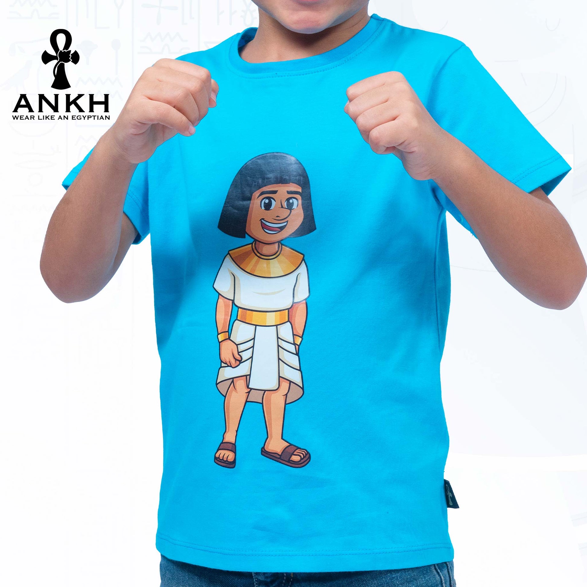 A child wearing a vibrant blue T-shirt adorned with a playful illustration of Sinuhe, an iconic Egyptian boy character - an epitome of luxury and cultural richness